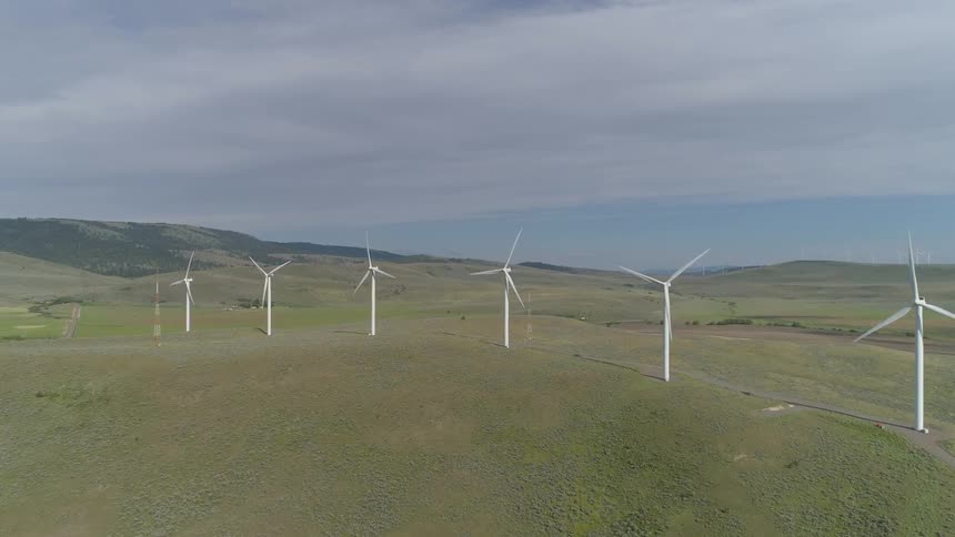 Wind turbines are spinning on top of a grassy hill