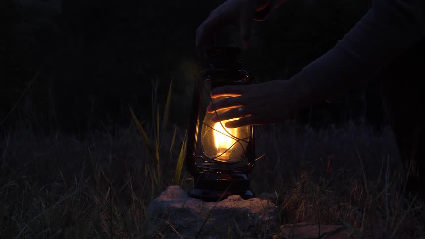 A person lighting a gas lantern wick and placing it on a rock