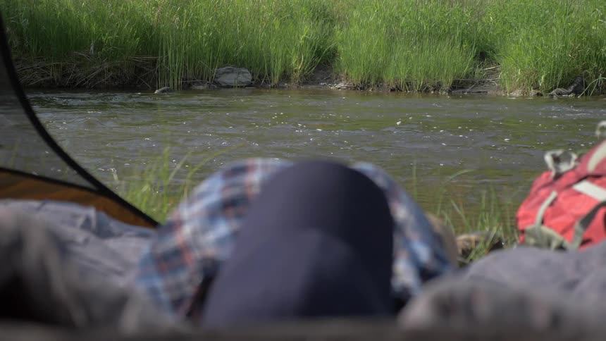 A person lays next to a flowing stream