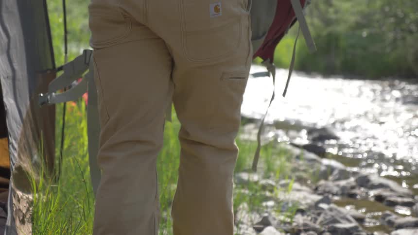 A man exiting a tent on a rivers edge while carrying a backpack