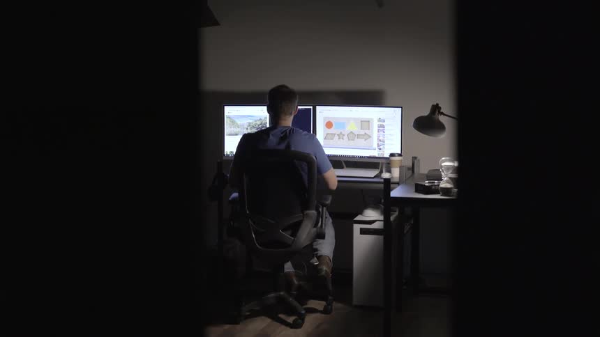 Man sitting at desk working on computer on a dim lit office