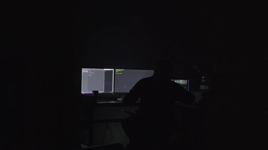 A person sits in a darkened room working on a computer