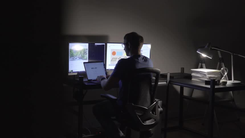 A man sits at his desk typing on a laptop
