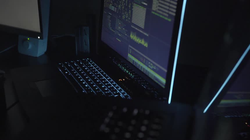 In a dark room a several computers are running with one rapidly cycling through a large quantity of graphs and data