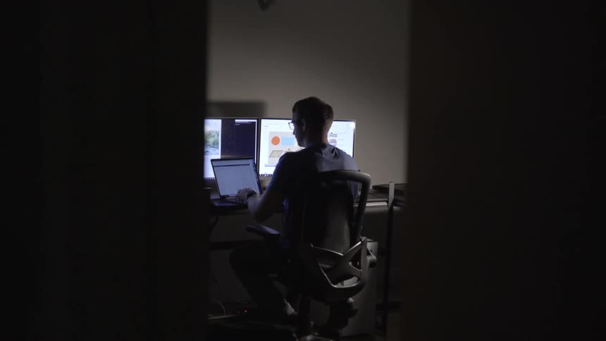 A man works on a laptop and two external monitors at a desk