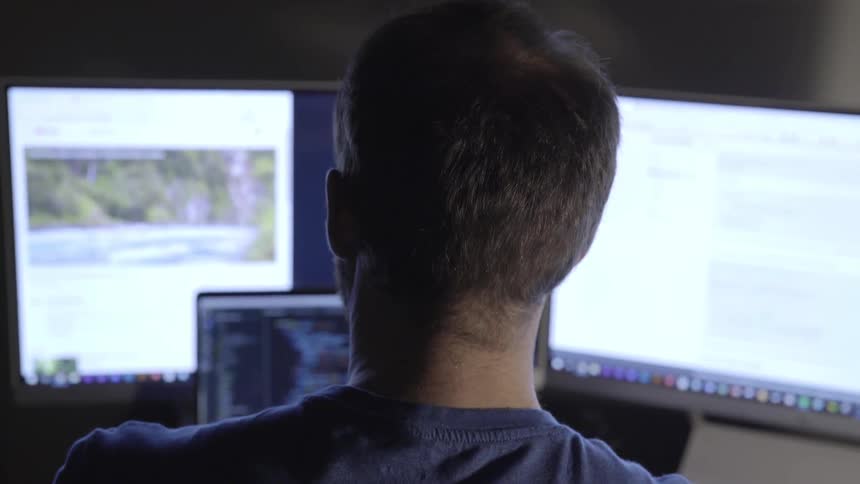 A man uses a laptop and two external monitors while sitting at a desk