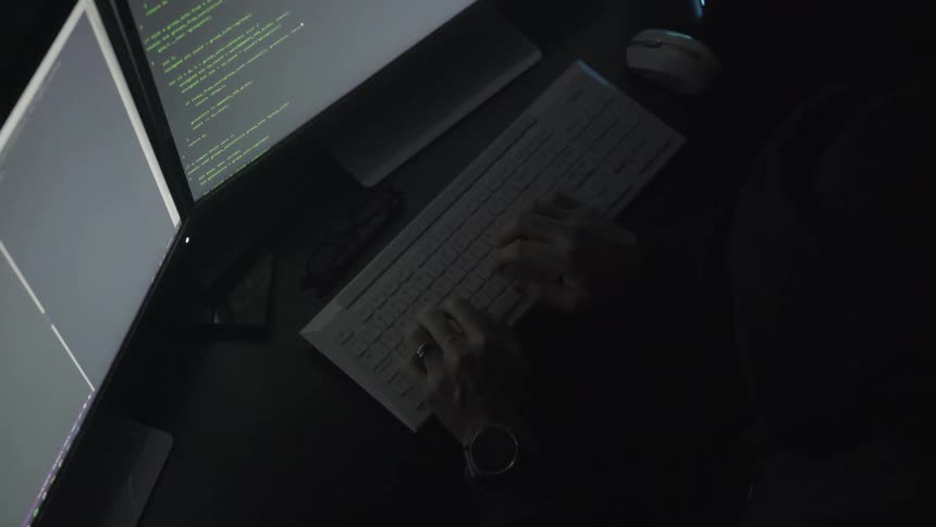 Man wearing wristwatch and ring types on a keyboard in a dark room at night