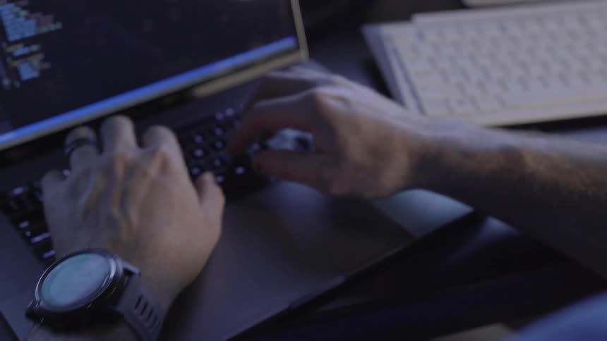A man is typing on a laptop and checks his smart watch