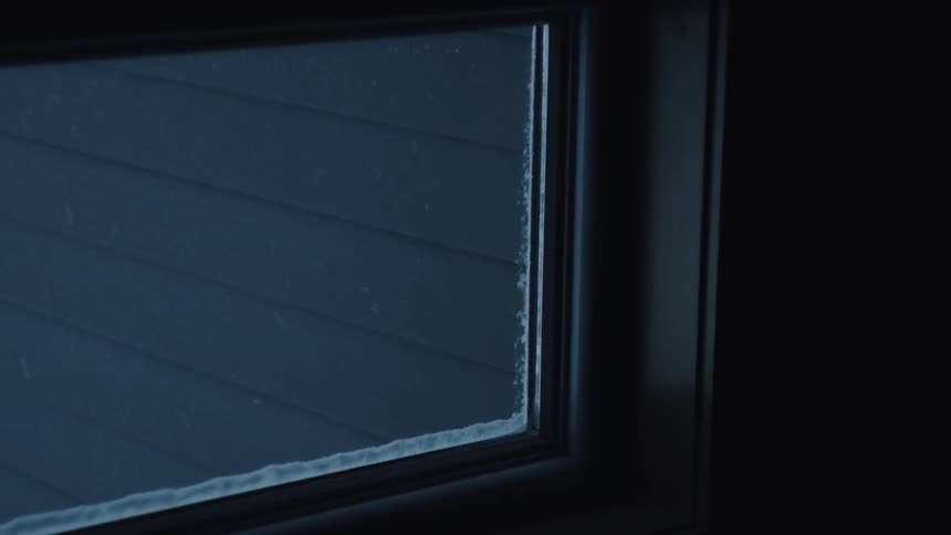 Snowflakes fall and gather on a houses window frame