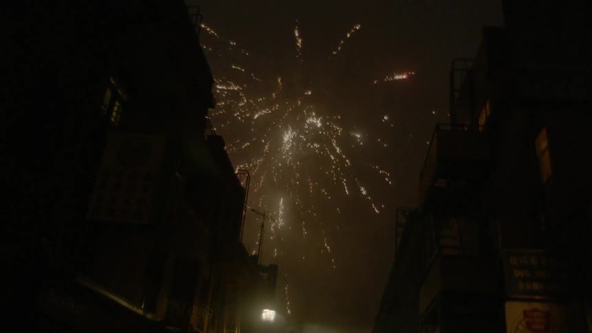 Fireworks explode over city buildings on a narrow street