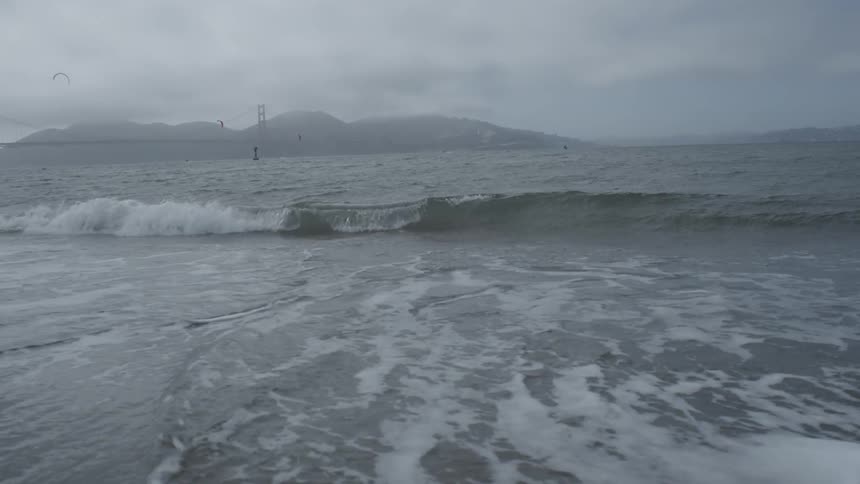 Waves crash on shore with mountains in the background