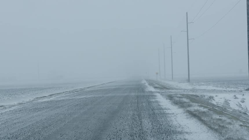 Snow blows across a rural road