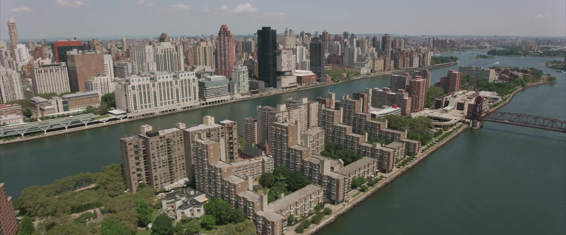 The camera flies over a river and bridge next to a dense city