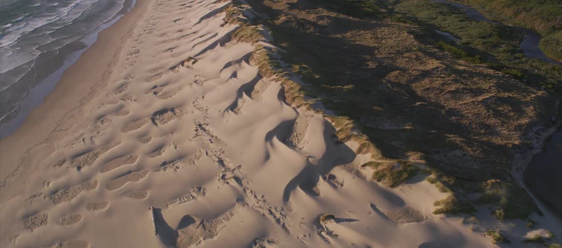 The camera looks down on sand next to the ocean