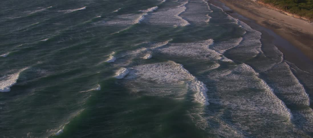 Aerial view of ocean waves gently crashing on a mountainous shoreline