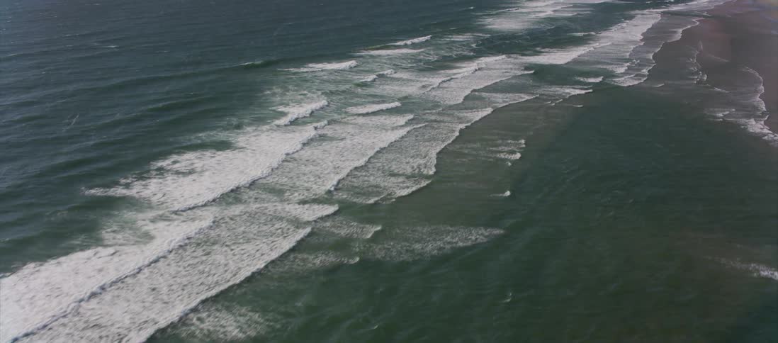 Camera flies over the coast with waves crashing against it