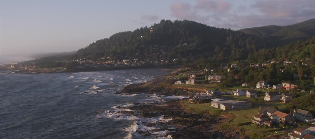 Waves crash against shore near town hugging mountains