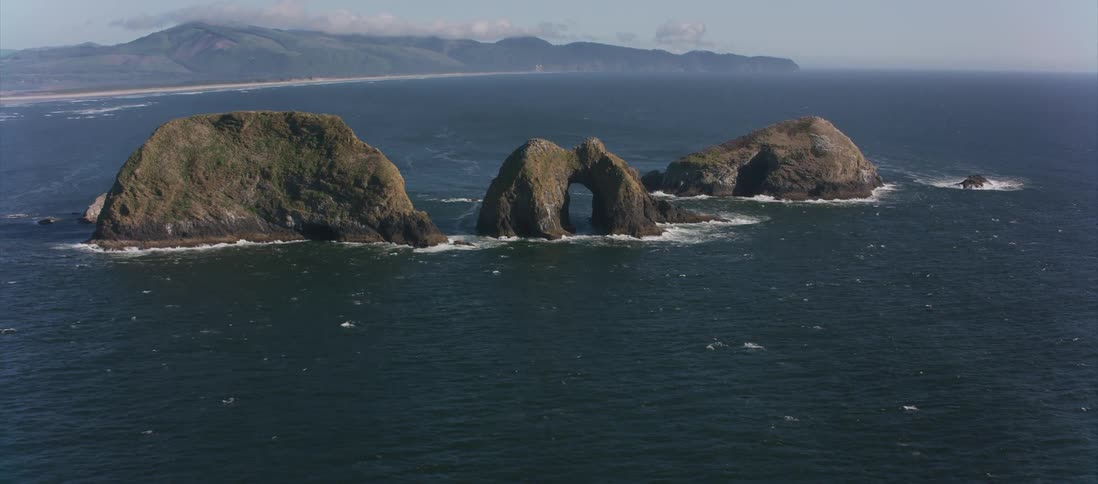 Mountains loom behind the deep blue ocean dotted with sea arches