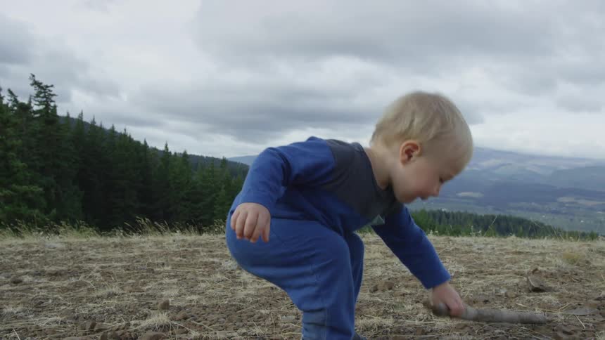A toddler holds a stick in the forest