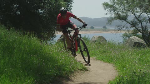 A man rides his mountain bike down a path near a lake