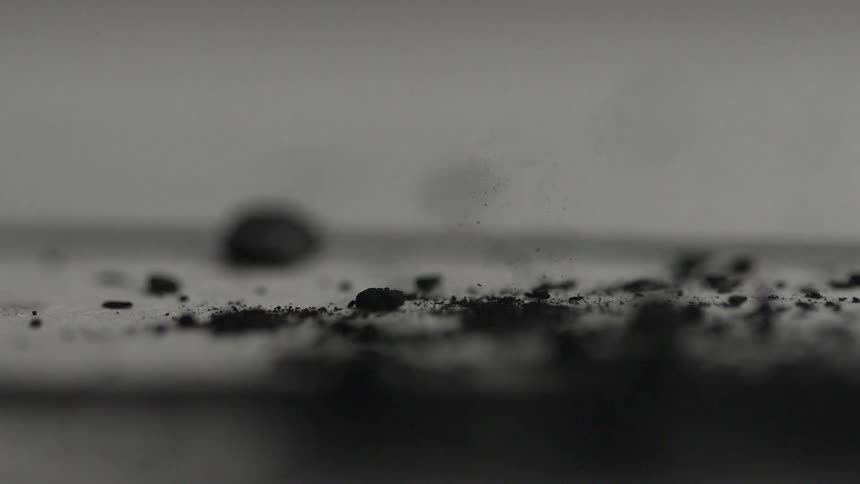Abstract closeup of bits of ash or charcoal dropping onto a surface