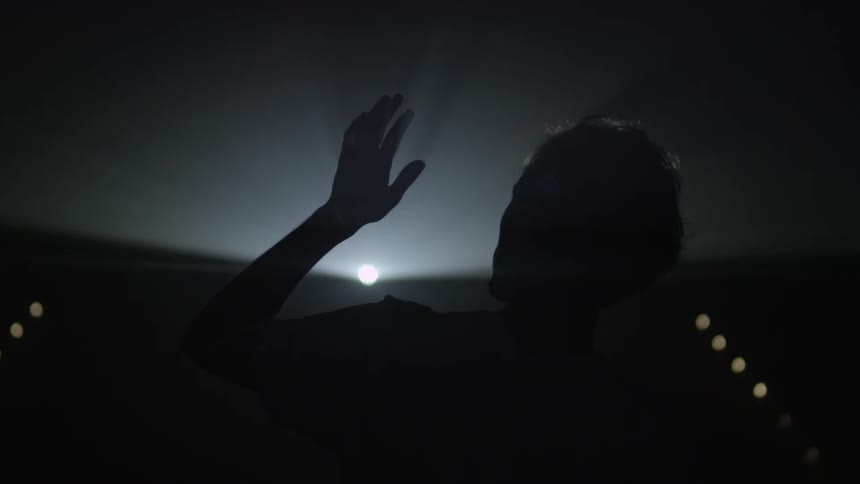 A silhouetted man stands in front of a strobing light