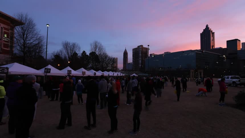 A crowd of people line up at outdoor tents while the sun rises