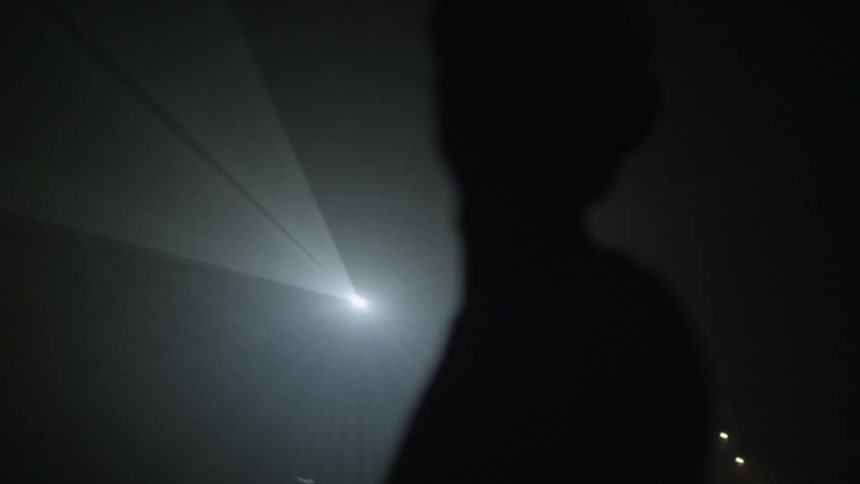 A young man walking back and forth as a strobe light shines behind him