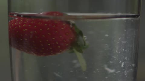 A strawberry falls into a glass and water