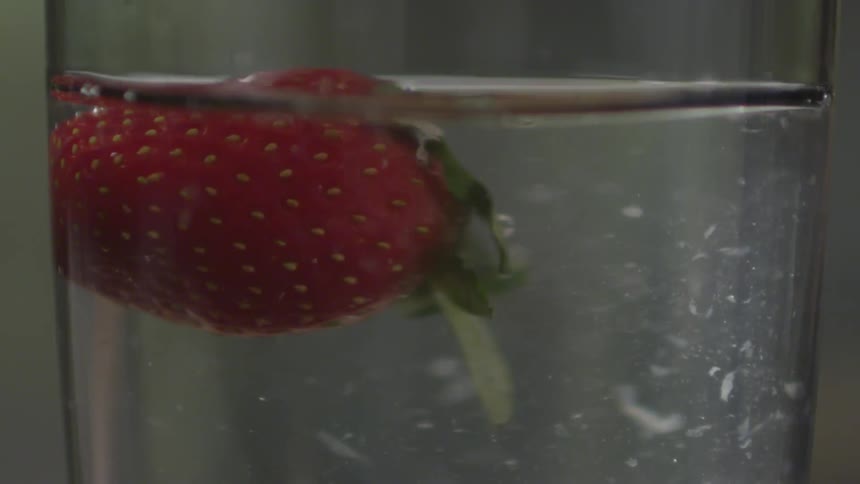 A strawberry falls into a glass and water