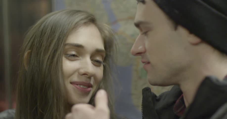 A man and a woman are standing close together and the man brushes the woman's hair away from her face