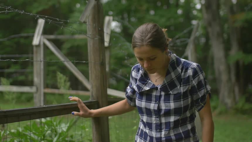 A woman walks along a barbed wire fence