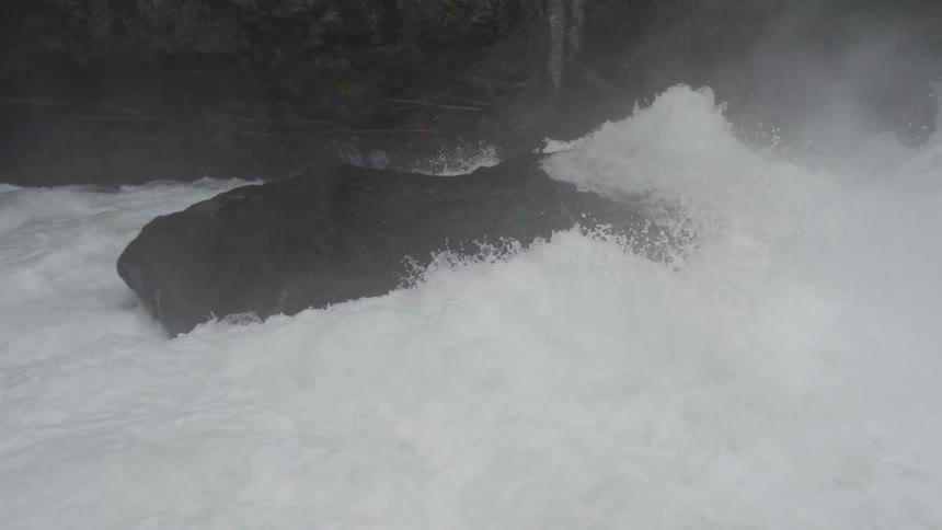 Handheld shot of a whitewater kayaker launching off a waterfall into the pool below and disappearing into the whitewater