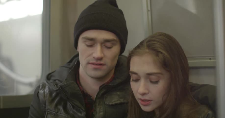 A couple sits next to each other holding hands on a train