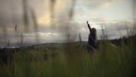 Girl in a field points up at a cloudy sky