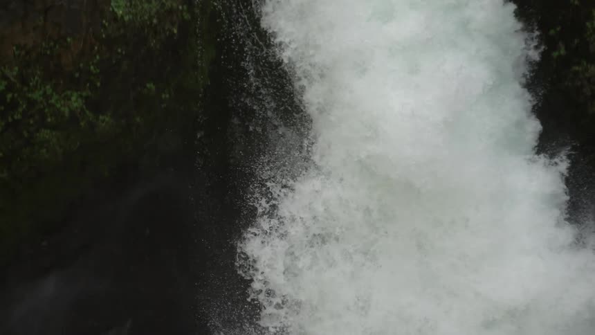 Slow motion shot tilting down following the water of Punchbowl Falls to the pool below