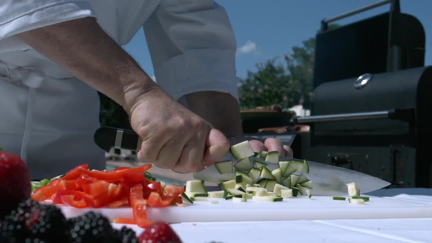 A chef cutting through vegetables while outside standing next to a grill