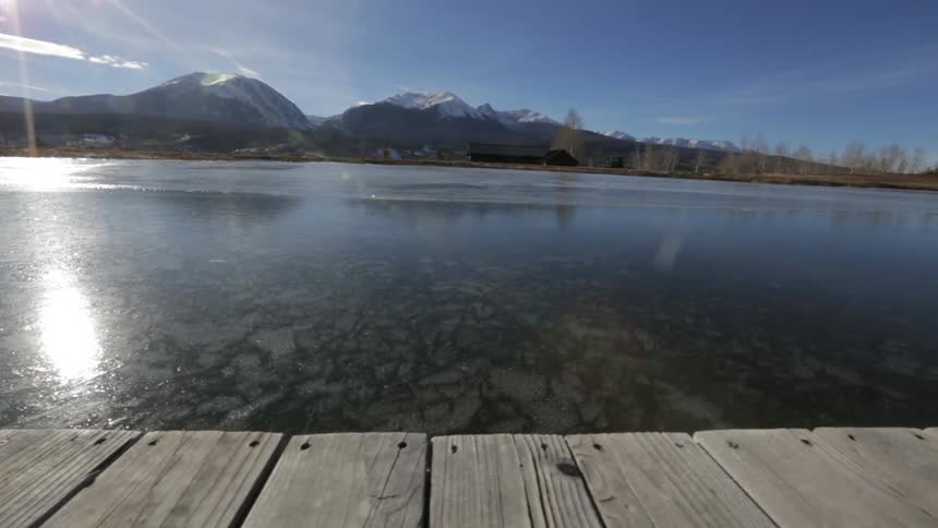 The sun reflects off of a calm body of water with mountains in the distance