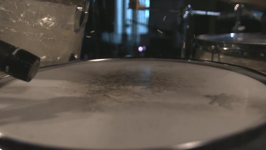 A drumstick hits the top of a drum