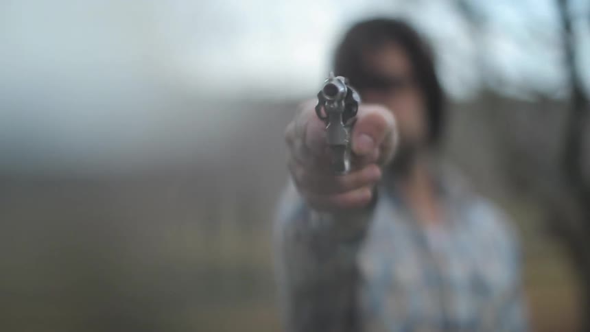 A man extends his arm pointing an unloaded revolver directly into the camera