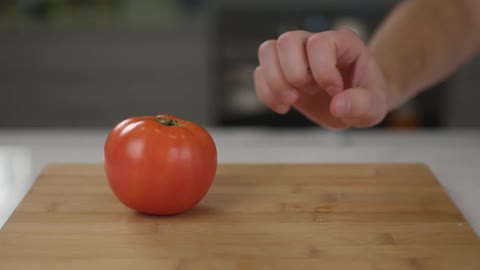 Someone grabbing two red tomatoes one at a time off a cutting board