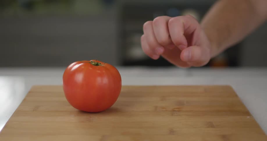 Someone grabbing two red tomatoes one at a time off a cutting board