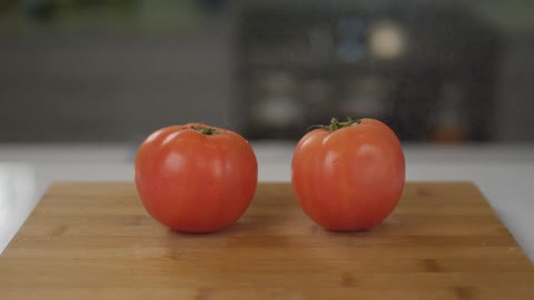 Mist sprays over two tomatoes on a cutting board
