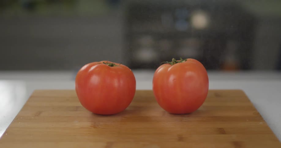 Mist sprays over two tomatoes on a cutting board