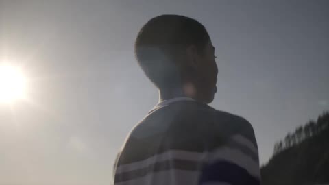 A young black boy runs on a beach with the sun shining brightly in the background