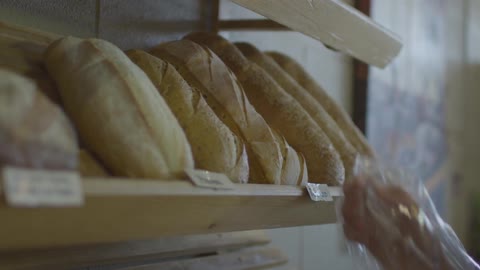 A person with food gloves on places baked bread on a shelf rack on the wall