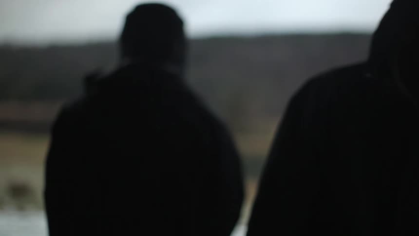 A man standing in the rain then turning around to hand something to someone who came up behind him