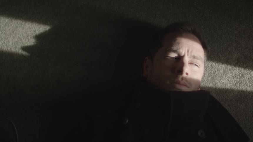 A man lays on the carpeted floor with sunlight shining across his face