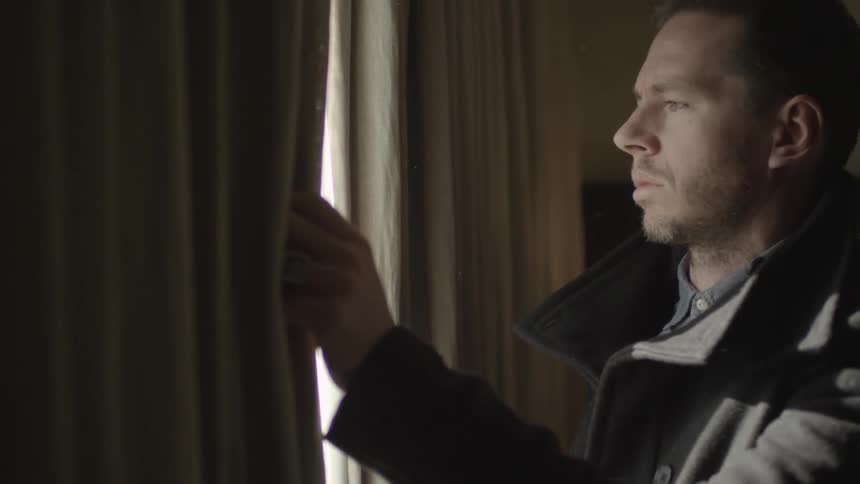 Man looks out of a curtain