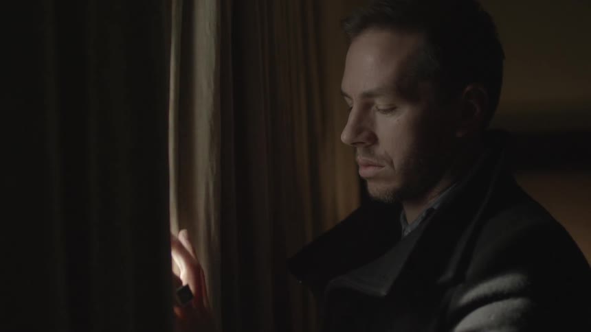 Man runs his hand down the curtains of the room